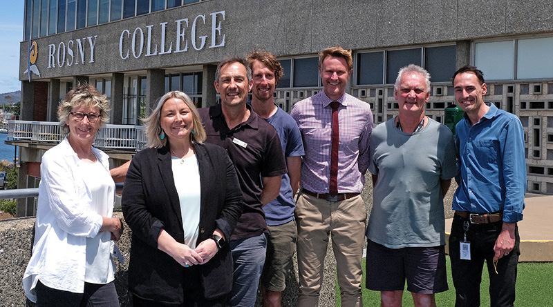 Former students and now Rosny Collage staff Cathy Ransom, Clare Latham, Gav Joyce, Callum Hollingsworth, Andrew Woodham, Ray Riewoldt and Tristan Ferguson standing in front of the Rosny Collage sign.